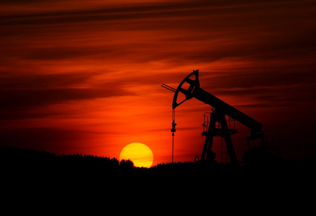 Silhouette of an oil pumpjack against a vibrant red sunset sky.
